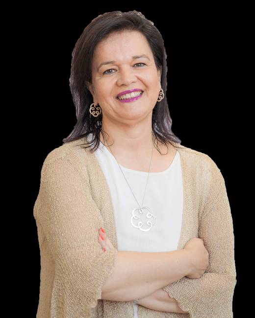 Una mujer sonriente con un suéter claro y con los brazos cruzados frente a un fondo negro.