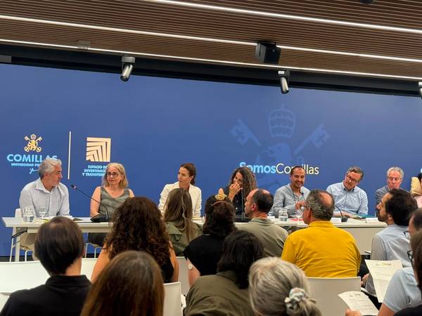 Una mesa redonda con varios ponentes y un público atento en un evento en la Universidad Comillas.