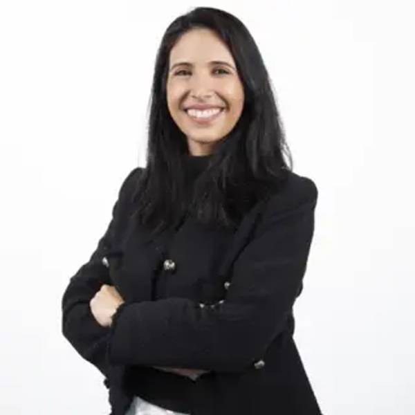 Una mujer sonriente con cabello largo oscuro viste una chaqueta negra y posa con los brazos cruzados.