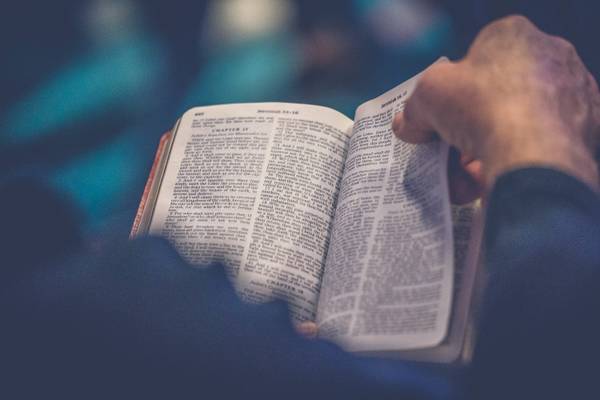 Una persona sostiene un libro abierto, probablemente una Biblia, mientras lee.