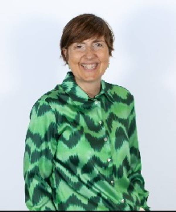 Una mujer sonriente viste una camisa verde con un patrón de zigzag.