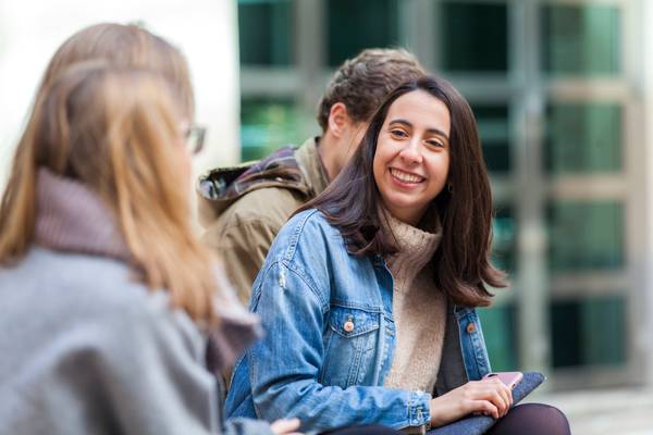 Un grupo de jóvenes se ríe y conversa al aire libre en un día soleado.
