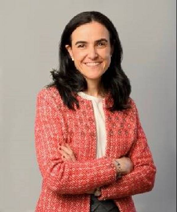 A woman in a red patterned jacket and white shirt, smiling with her arms crossed.