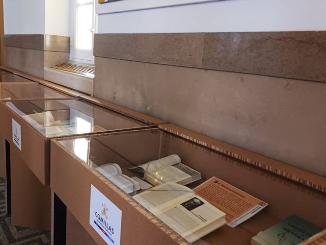 La imagen muestra una exposición con vitrinas de libros y documentos en un ambiente iluminado.