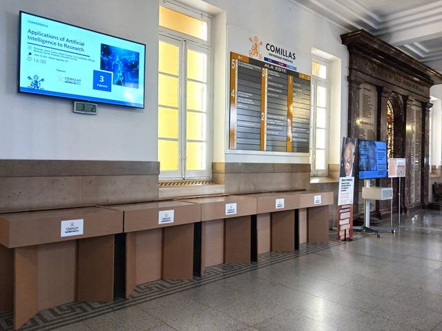Interior de un edificio con pantallas y paneles informativos sobre un evento relacionado con la inteligencia artificial.