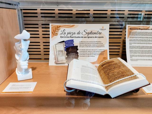 La imagen muestra una exposición con un libro abierto y una figura blanca al lado, que están relacionados con los Ejercicios Espirituales de San Ignacio de Loyola.