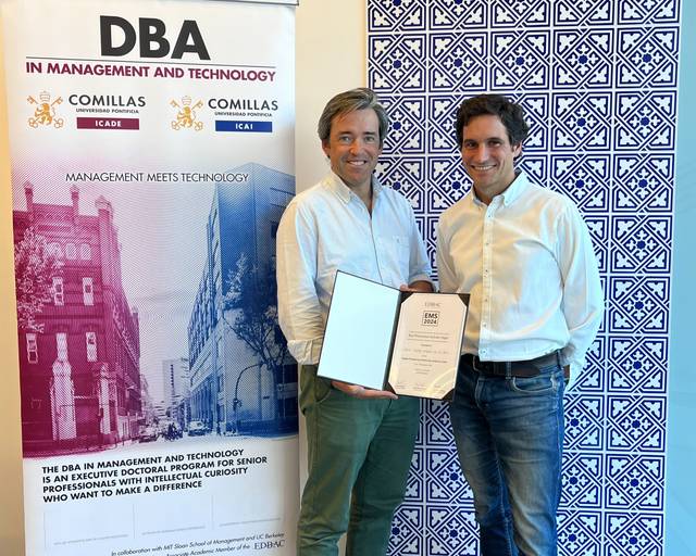 Two men in business casual attire standing in front of a promotional banner for DBA in Management and Technology, holding a certificate.