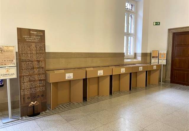 La imagen muestra una serie de cajas de cartón dispuestas en un espacio interior junto a un panel informativo.