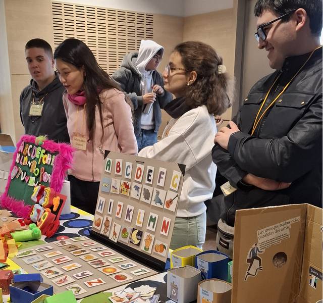Un grupo de personas observa una mesa con materiales educativos y colores vibrantes.