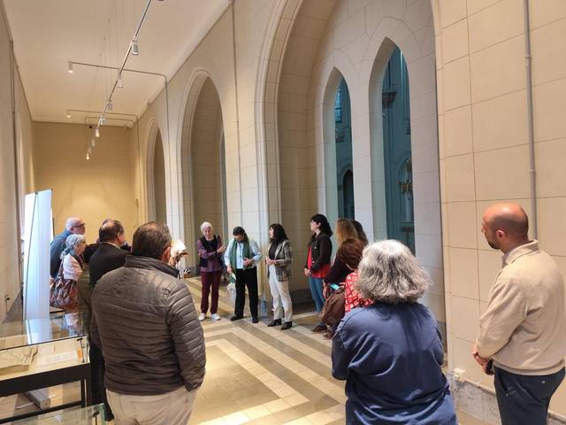 Un grupo de visitantes se encuentra en un museo, observando una presentación ante una guía.