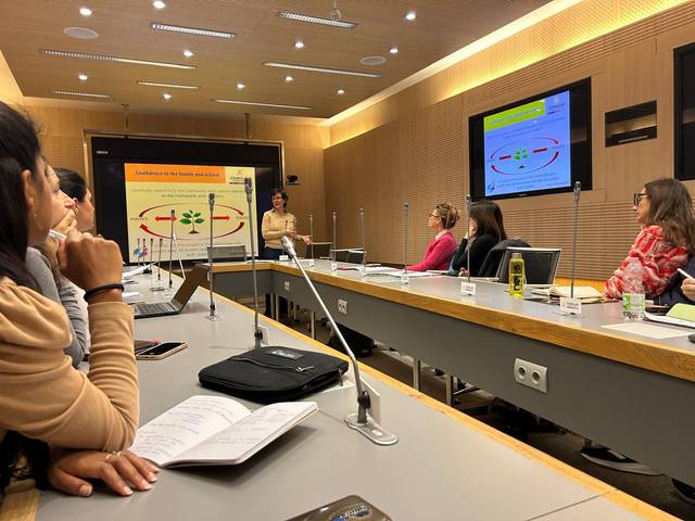 Una presentación en una sala de conferencias con varias personas escuchando a una ponente frente a una pantalla.