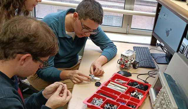 Tres estudiantes trabajan colaborativamente en el ensamblaje de un robot utilizando piezas y herramientas adecuadas.