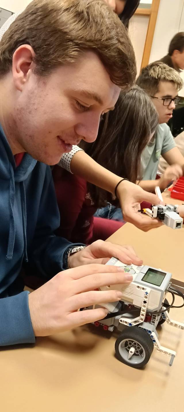 Un grupo de estudiantes trabaja en un proyecto de robótica, programando un robot con control remoto.