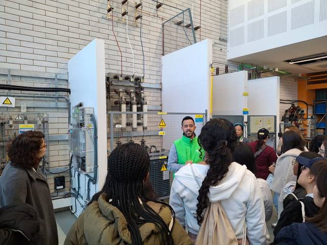 Un grupo de estudiantes escucha atentamente a un instructor durante una visita técnica en un laboratorio.