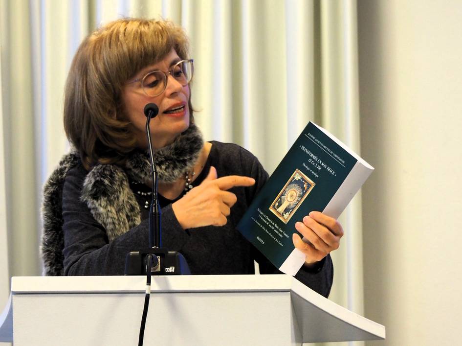 Una mujer presenta un libro mientras señala su portada con entusiasmo.