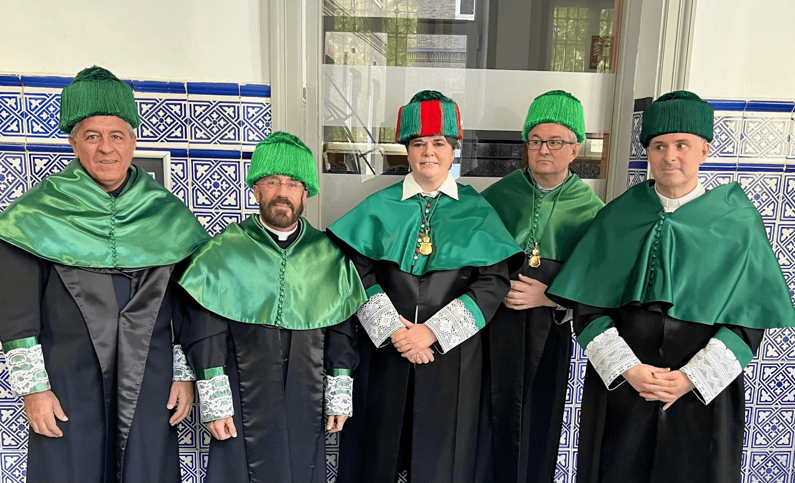 Un grupo de cinco personas vestidas con togas y gorros verdes en un entorno que recuerda a una ceremonia formal.